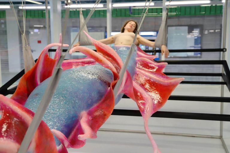 Frau hängt in einem Raum mit rot-blauem Fisch-Kostüm am Unterkörper